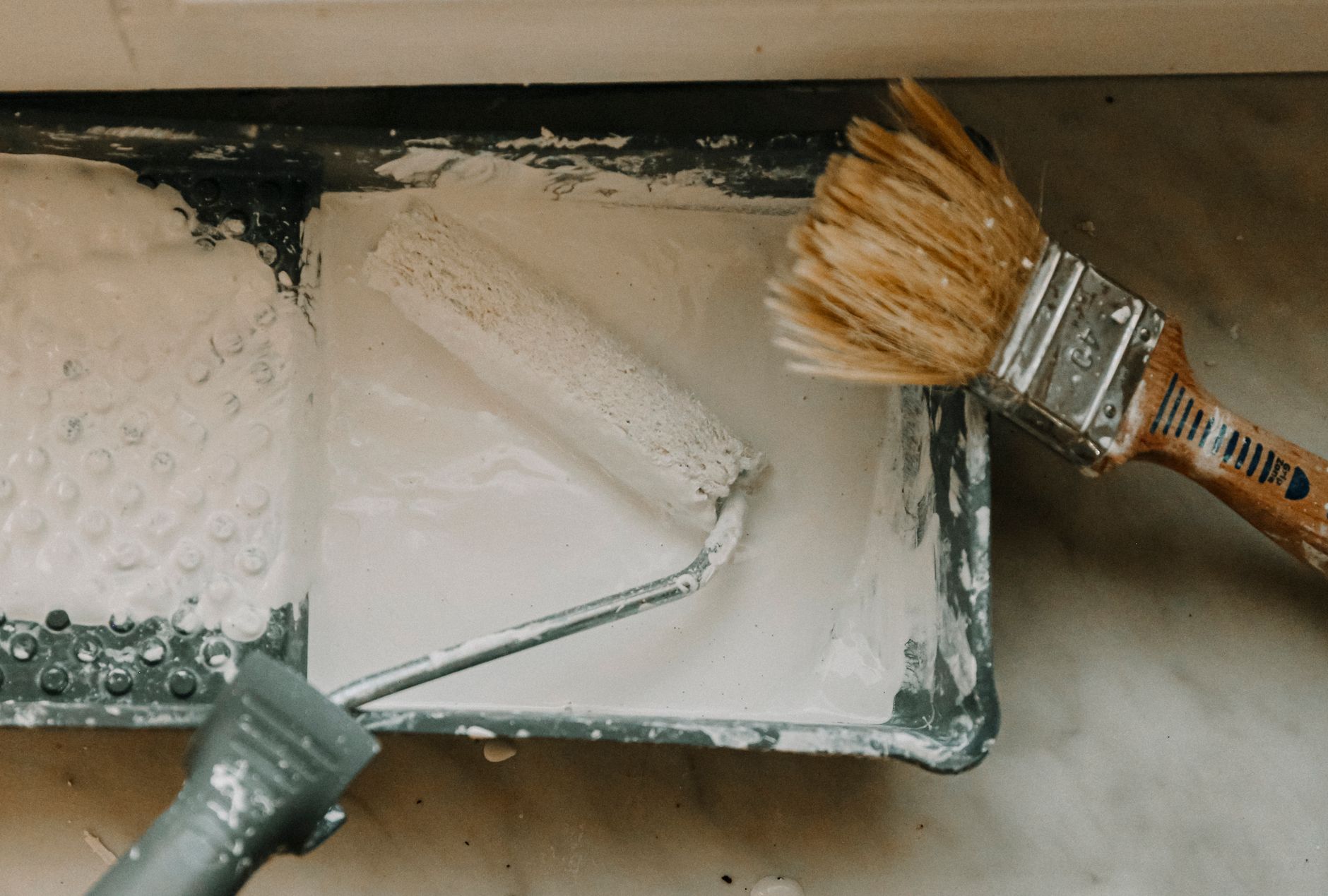 Overhead view of a paint roller and brush in a tray with white paint. Perfect for DIY and home renovation in Riverside, CA
