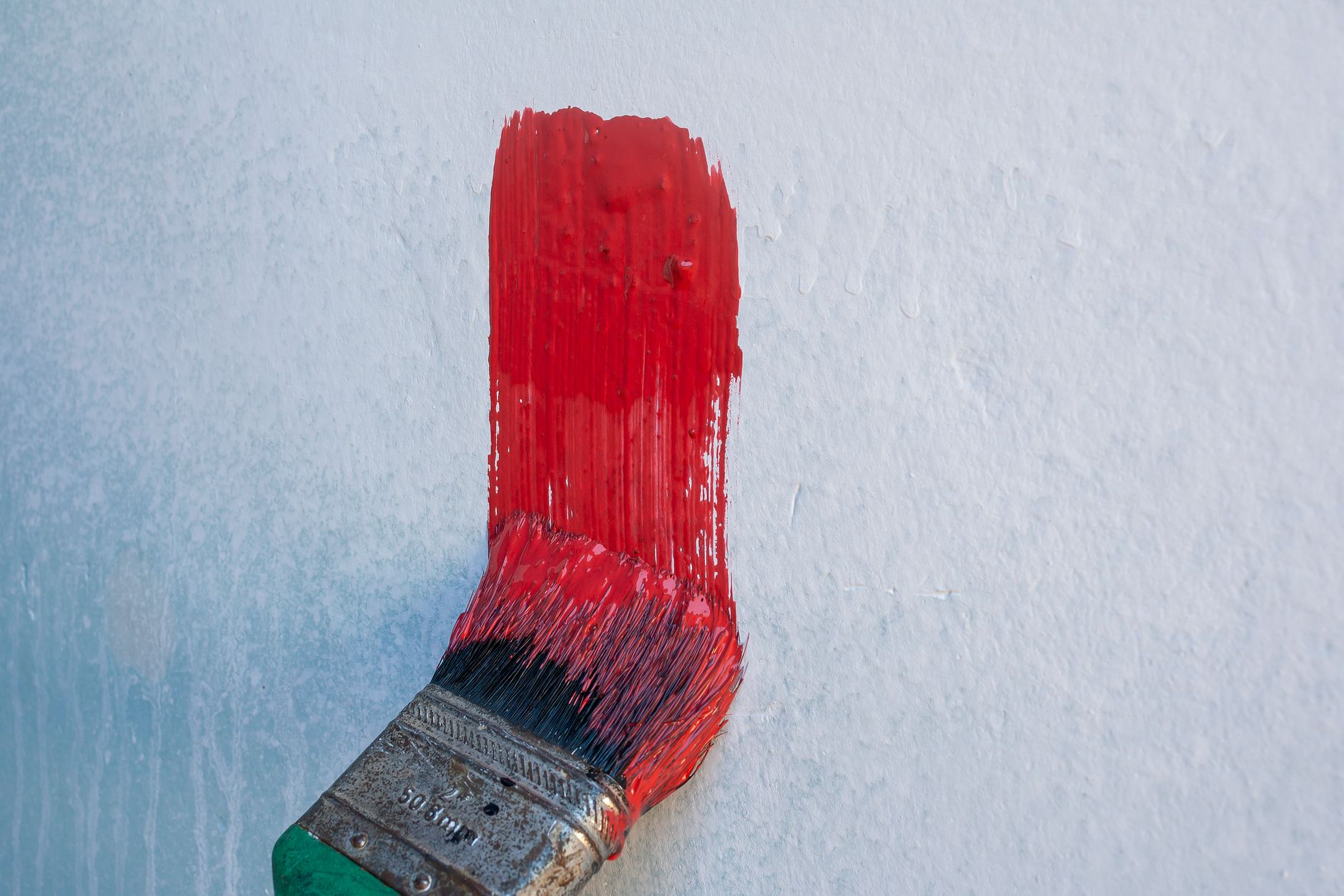 A paintbrush applies vibrant red paint to a white wall, showcasing DIY home improvement in Riverside, CA