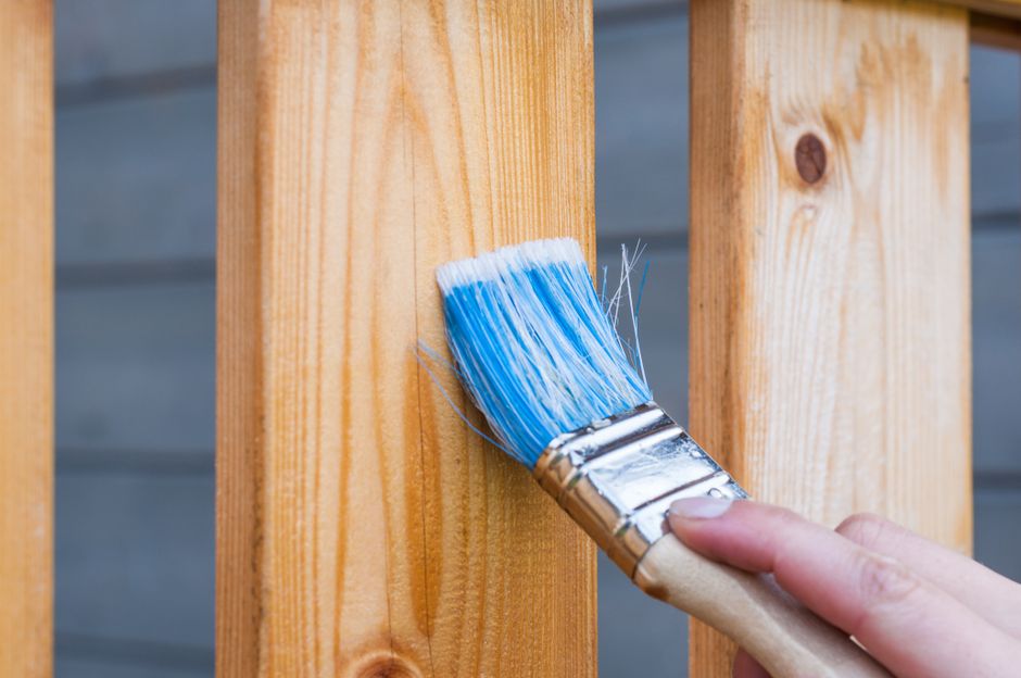 A hand painting a wooden board with a blue paintbrush.