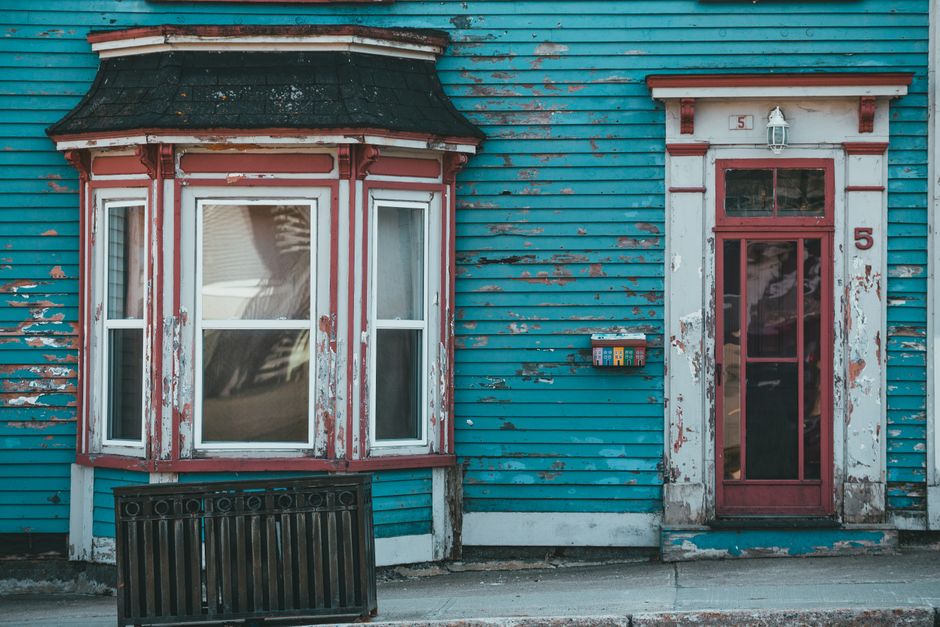 Weathered blue painted wall with a bow window and a door.