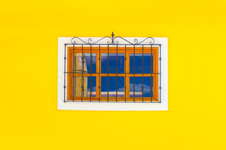 Small window with a wooden frame set in a yellow painted wall.
